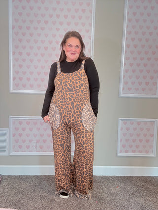 Person wearing a leopard print overalls in a room with patterned wallpaper.