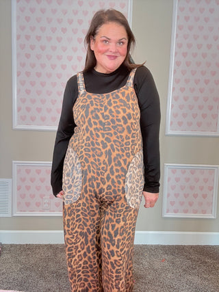 Person wearing a leopard print overalls in a room with pink heart wallpaper.