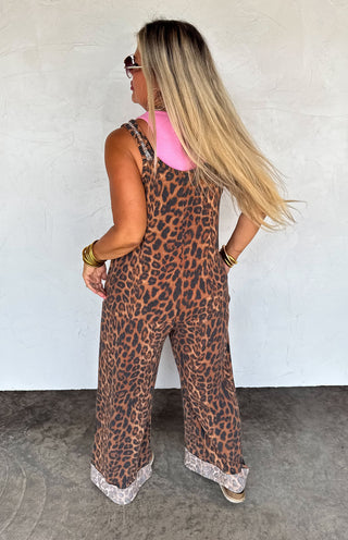 Woman wearing a leopard print jumpsuit with lace trim against a white wall.