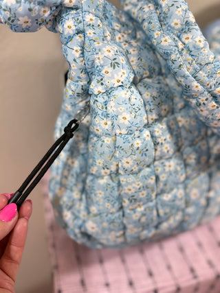 Blue Ditsy Floral Quilted Bag with a charming floral print, secure zipper closure, water-resistant inner lining, multiple pockets, and a comfortable shoulder strap—perfect for everyday use or travel.