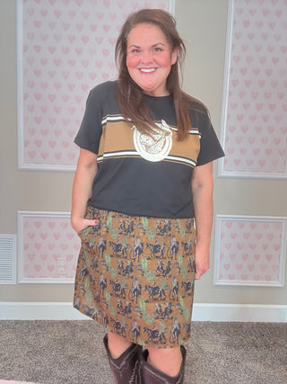 Woman wearing a black t-shirt with a graphic design and a western patterned skirt in a room with heart-shaped decorations on the walls.