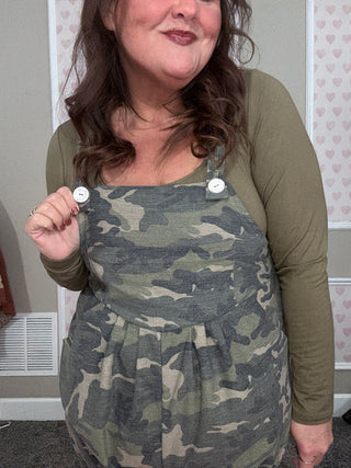 Person wearing a camouflage dress with a green jacket indoors.