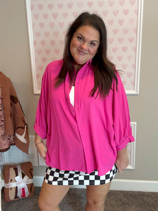 Woman wearing a pink blouse and checkered skirt standing in a room with heart-patterned wallpaper.