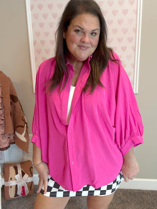 Woman wearing a bright pink shirt over a white top with a checkered skirt in a room.