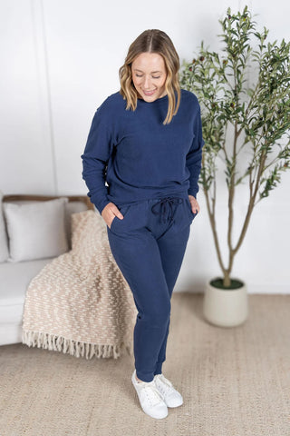 Model wearing the Corrine Ribbed Pullover in navy, styled with matching ribbed joggers. Features crew neckline, ribbed texture, and relaxed fit.