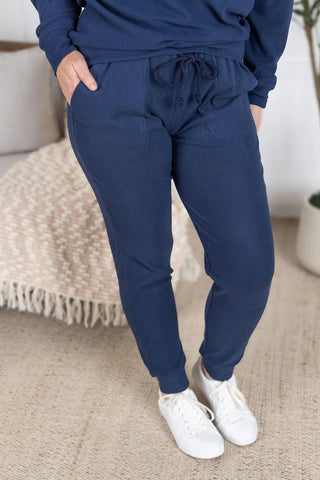 Model wearing navy ribbed joggers with drawstring waist and cuffed ankles, paired with matching pullover, standing casually outdoors.