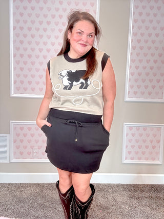Woman wearing a sleeveless top with a graphic design and a black skirt in a room with heart-patterned wallpaper.