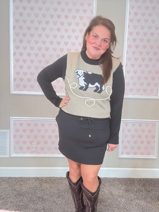 Person wearing a sweater with a dog graphic and skirt in a room with heart-patterned wallpaper.