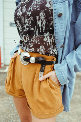 Mid-rise saddle brown corduroy shorts with cuffed hem and buckstitch pocket detailing. Western-inspired style with a modern, flattering fit.
