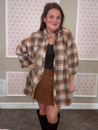 Woman wearing a plaid flannel over a brown skort in a room with patterned wallpaper.
