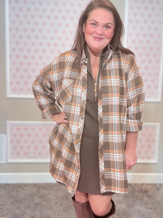 Woman wearing a plaid flannel over a dress with a neutral background