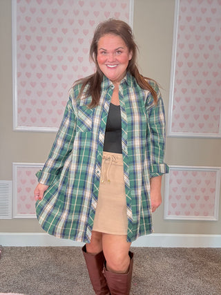 Person wearing a green plaid flannel with ribbed beige skort in a room with patterned wallpaper.