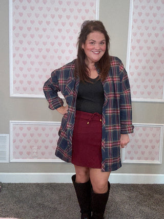 Person wearing a plaid flannel over a burgundy skort in front of a patterned wall.