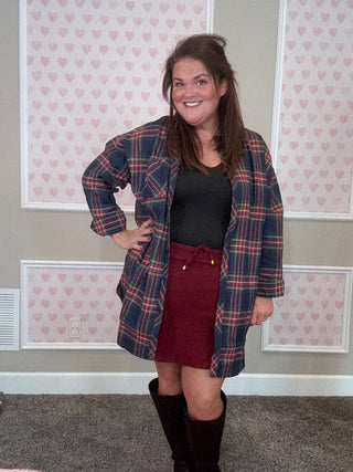 Person wearing a plaid flannel and burgundy skort in a room with patterned wallpaper.