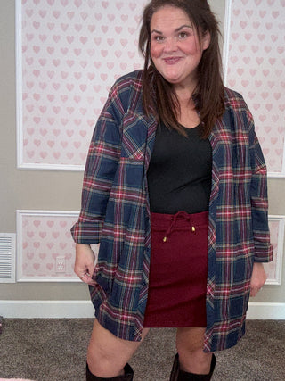 Person wearing a plaid flannel over burgundy skort in a room with patterned wallpaper