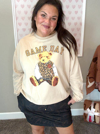 Person wearing a 'Game Day' sweatshirt with a bear graphic in a room with heart-patterned wallpaper.
