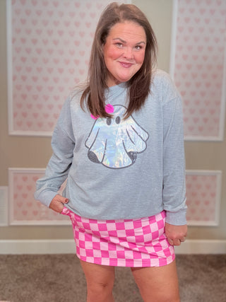 Person wearing a gray sweatshirt with a cartoon design and a pink checkered skirt in a room with heart-patterned wallpaper.