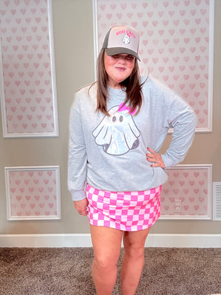 Person wearing a gray sweatshirt with a cartoon design, pink checkered skirt, and cap indoors.