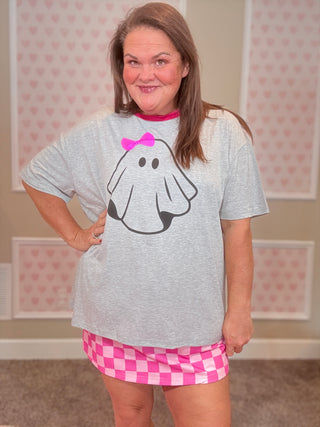Person wearing a gray t-shirt with a ghost design and pink shorts in a room with heart-patterned wallpaper.