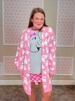 Person wearing a pink sweater with white cat patterns in a room with heart-patterned wallpaper.