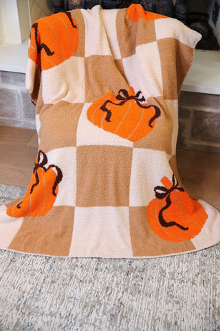 Checkered blanket with orange pumpkins and black stems on a wooden floor.