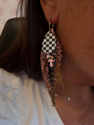 Close-up of a person wearing a checkered feather earring with glittery details.