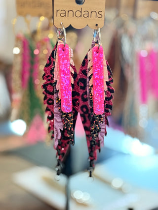 Layered faux leather earrings with a bold hot pink glitter bar on top, pink paisley and leopard print layers underneath, finished with dangling black chain links. Hanging on a “randans” branded card.