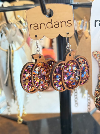 Wooden pumpkin-shaped earrings filled with chunky fall-toned glitter in orange, pink, and gold. Displayed on a “randans” earring card.