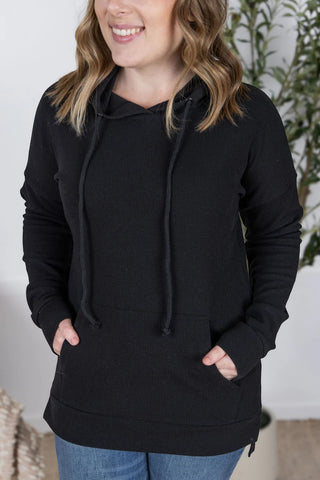 Woman wearing the black Kacey Ribbed Hoodie styled with leggings, showing the front slit and relaxed fit.