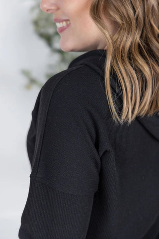 Close-up of ribbed fabric and cuffed sleeve of the Kacey Hoodie in black, with subtle texture visible.