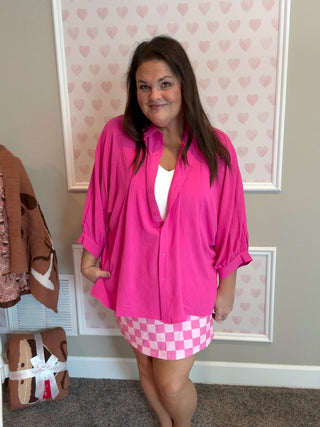 Woman wearing a bright pink blouse and checkered skirt in a room with heart-patterned wallpaper.