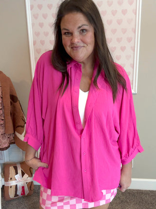 Woman wearing a bright pink shirt with a checkered skirt in a room with heart-patterned wallpaper.