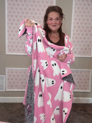 Person holding a pink blanket with ghost patterns in a room with heart-patterned wallpaper.