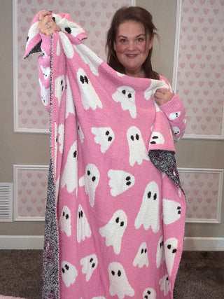 Person holding a pink blanket with ghost patterns in a room with heart-shaped wallpaper.