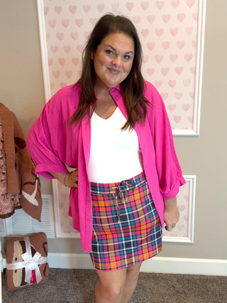 Woman wearing a pink cardigan, white top, and plaid skirt in a room with heart-patterned wallpaper.