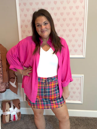 Woman wearing a pink shirt and plaid skirt in a room with heart-patterned wallpaper.