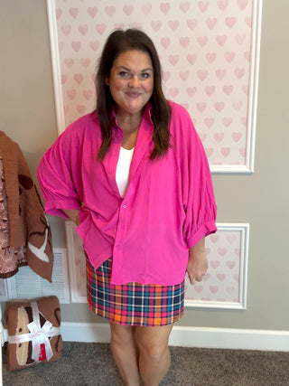 Woman wearing a pink blouse and plaid skirt standing in a room with heart-patterned wallpaper.
