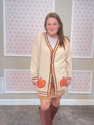 Woman wearing a beige cardigan with pumpkin designs in a room with heart-patterned wallpaper.