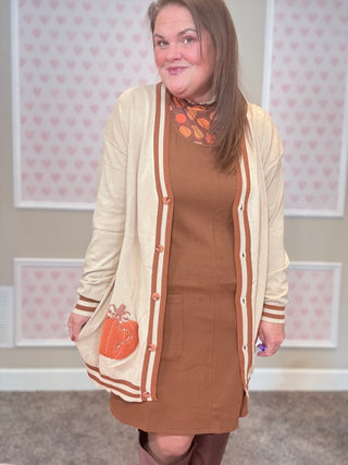 Woman wearing a brown dress with a beige cardigan in a room with heart-patterned wallpaper.