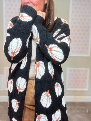 Person wearing a black cardigan with white and orange pumpkins, standing indoors.