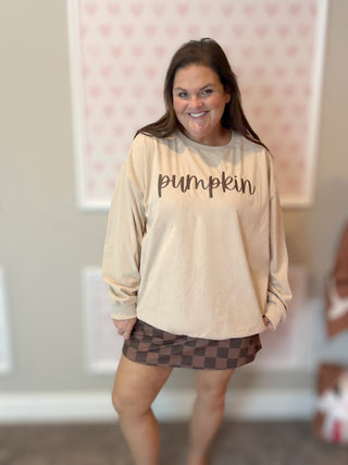 Woman wearing a beige 'pumpkin' shirt in a room with a pink heart-patterned wall.