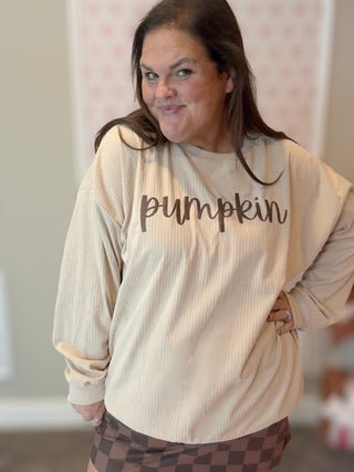 Person wearing a beige ribbed long-sleeve shirt with 'pumpkin' text.