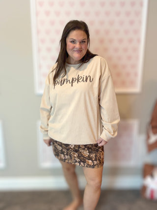 Woman wearing a beige sweatshirt with 'pumpkin' text in a room with a pink wall.