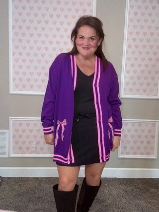 Person wearing a purple jacket with pink accents and black shorts in a room with patterned wallpaper.