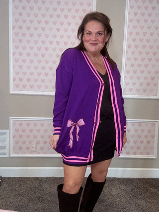 Person wearing a purple cardigan with pink accents in a room with patterned wallpaper.