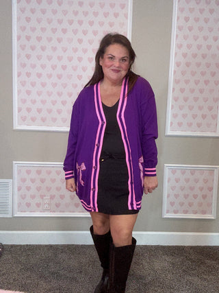 Person wearing a purple and pink cardigan in a room with patterned wallpaper.