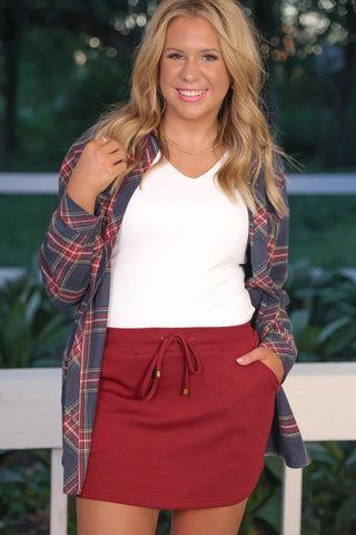 Woman wearing a plaid shirt over a white top and red skirt outdoors.