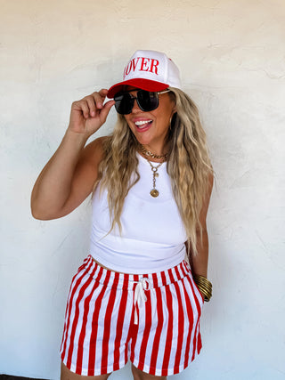 Model wearing red and white striped shorts with elastic waistband and drawstring, paired with a white tank top.