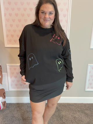 Person wearing a black sweatshirt with ghost designs in a room with heart-patterned wallpaper.