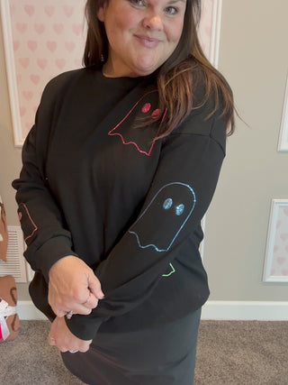 Person wearing a black sweatshirt with ghost designs in a room.